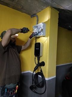 Un hombre está instalando una estación de carga en una pared amarilla.
